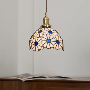 Stained glass pendant light with blue and cream daisy design above wooden side table and magazine, interior lighting