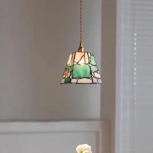 Stained glass pendant light installed in residential interior, low-angle view showing twisted hanging cord and warm ambient glow