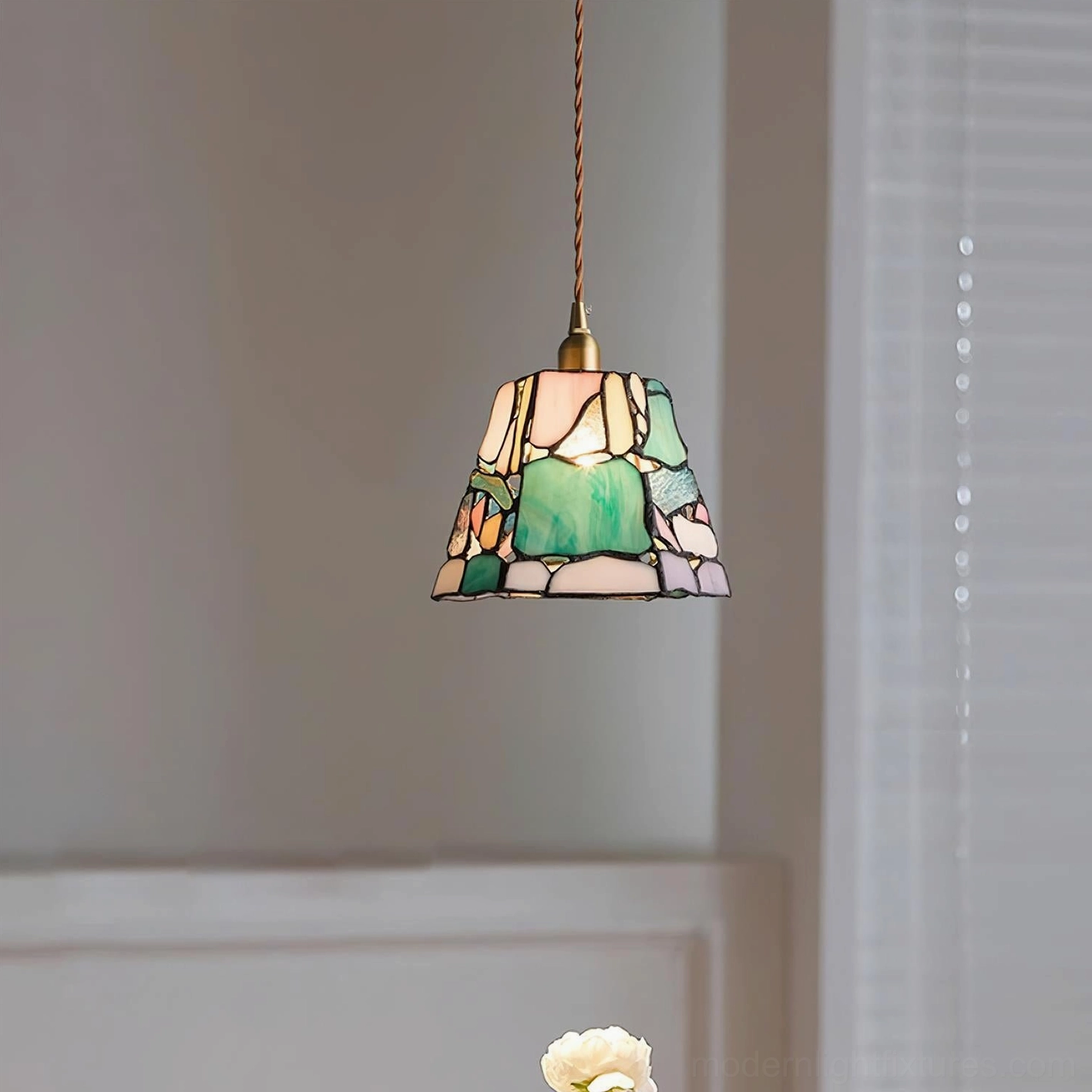 Stained glass pendant light installed in residential interior, low-angle view showing twisted hanging cord and warm ambient glow