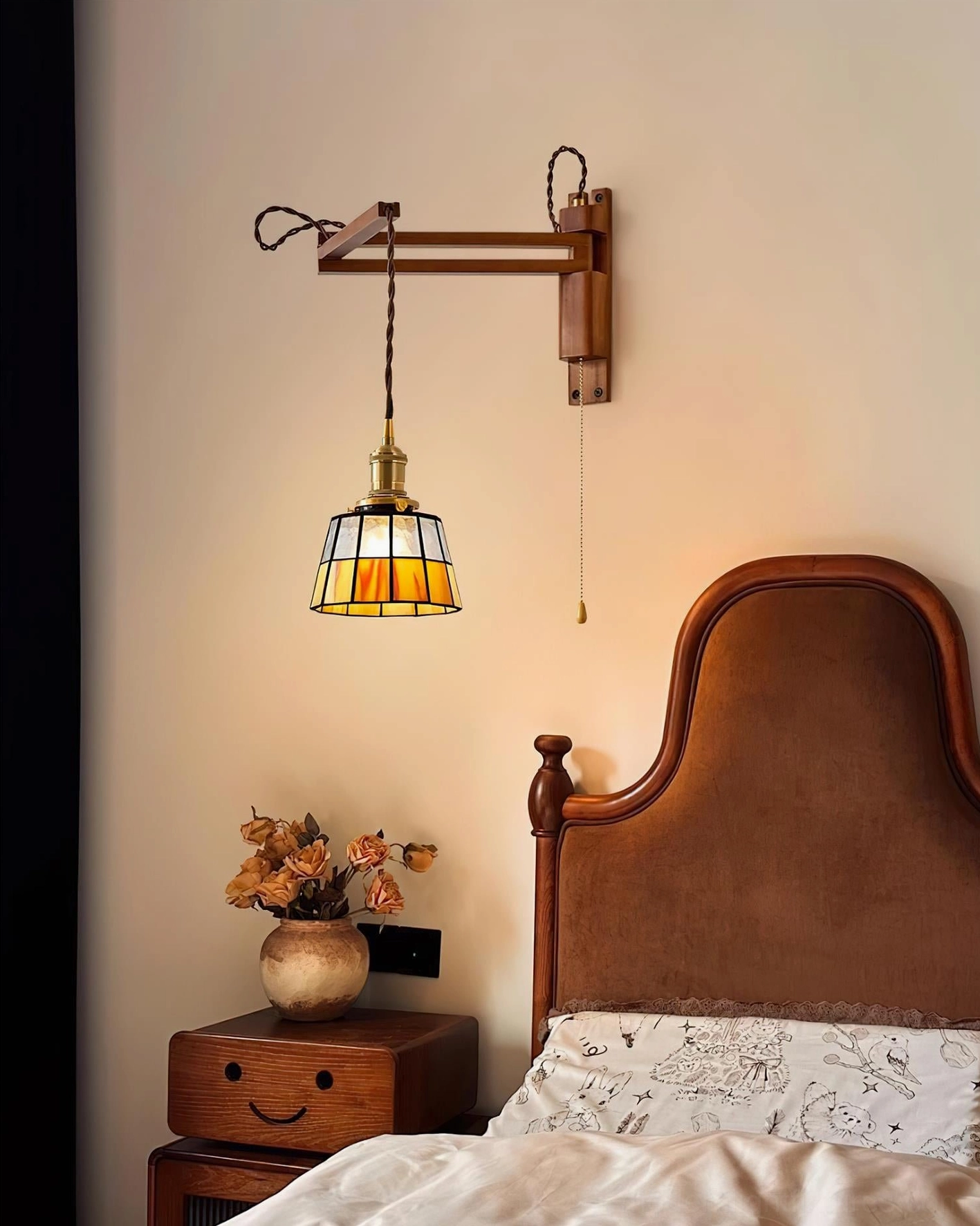 Tiffany-style wall sconce with geometric stained glass shade installed in modern bedroom above curved headboard, illuminated warm light diffusing through glass