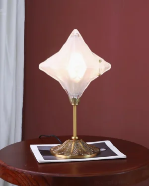 Illuminated Stellara table lamp on wooden side table with burgundy wall, ornate brass base, soft diffused lighting, contemporary home decor