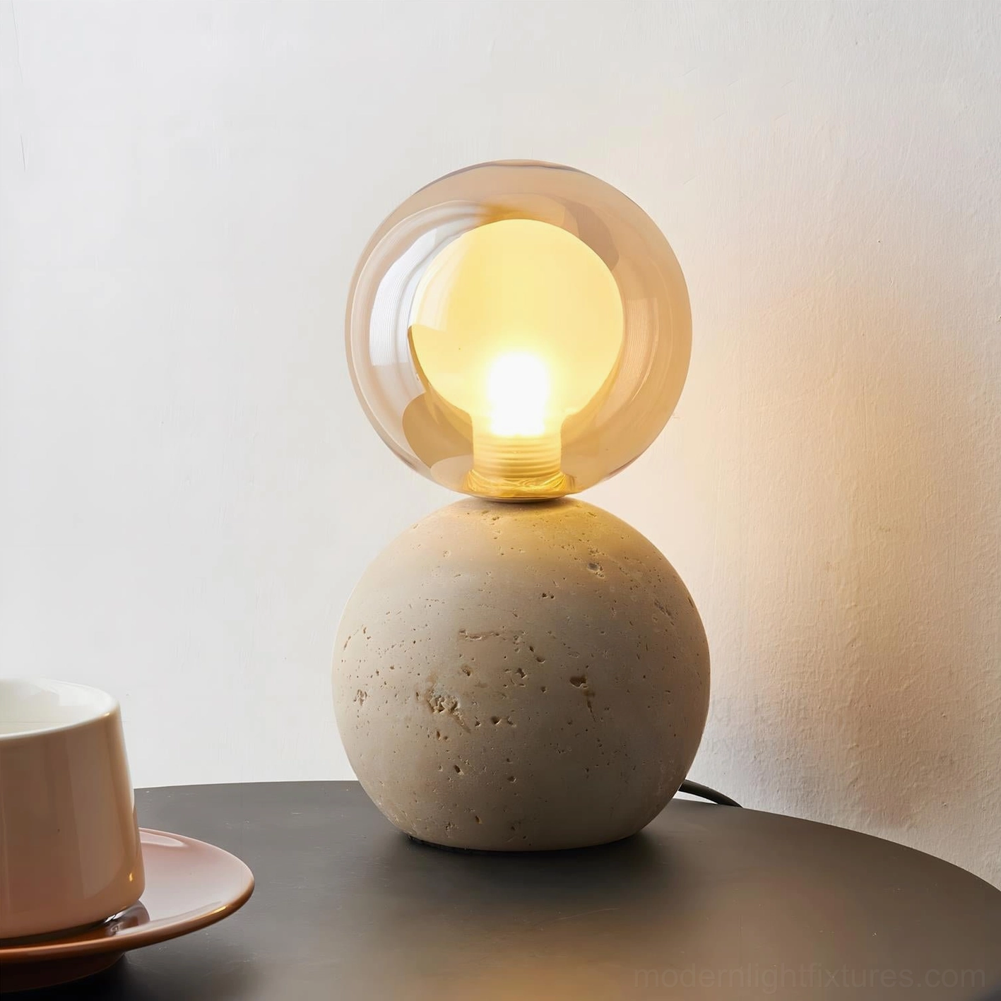 Hand-carved travertine spherical table lamp with exposed bulb glowing warm ambient light