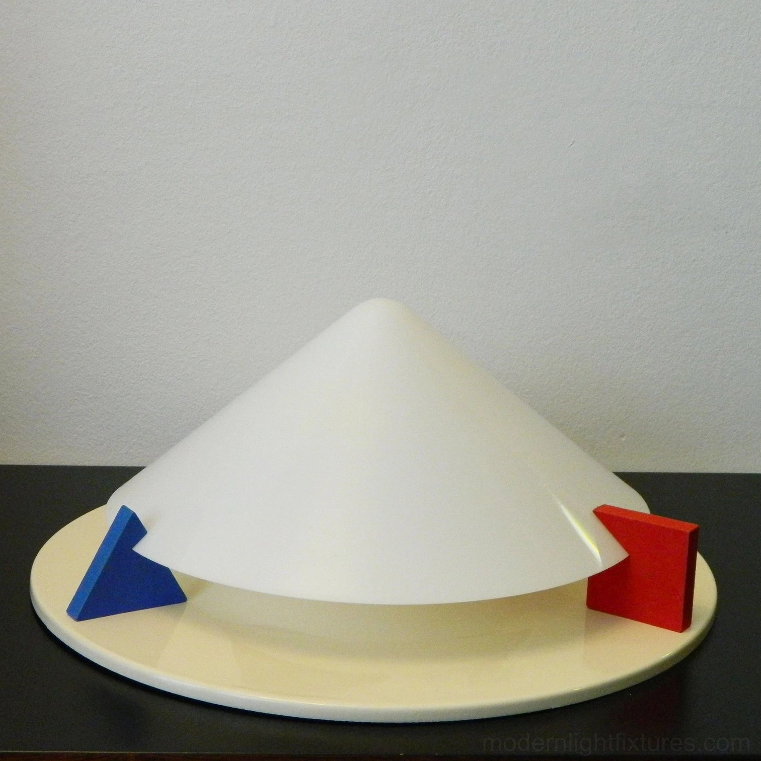 Stoja tabletop display lamp low front angle shot showing cream round base with blue and red Memphis design accent blocks
