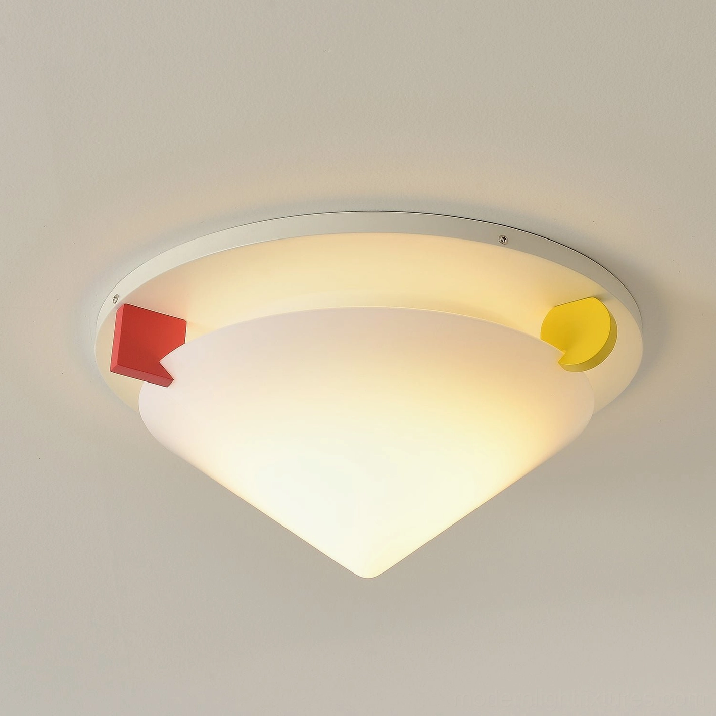 Stoja flush mount ceiling lamp lit close-up with warm lighting showcasing red and yellow geometric accent blocks against plain backdrop