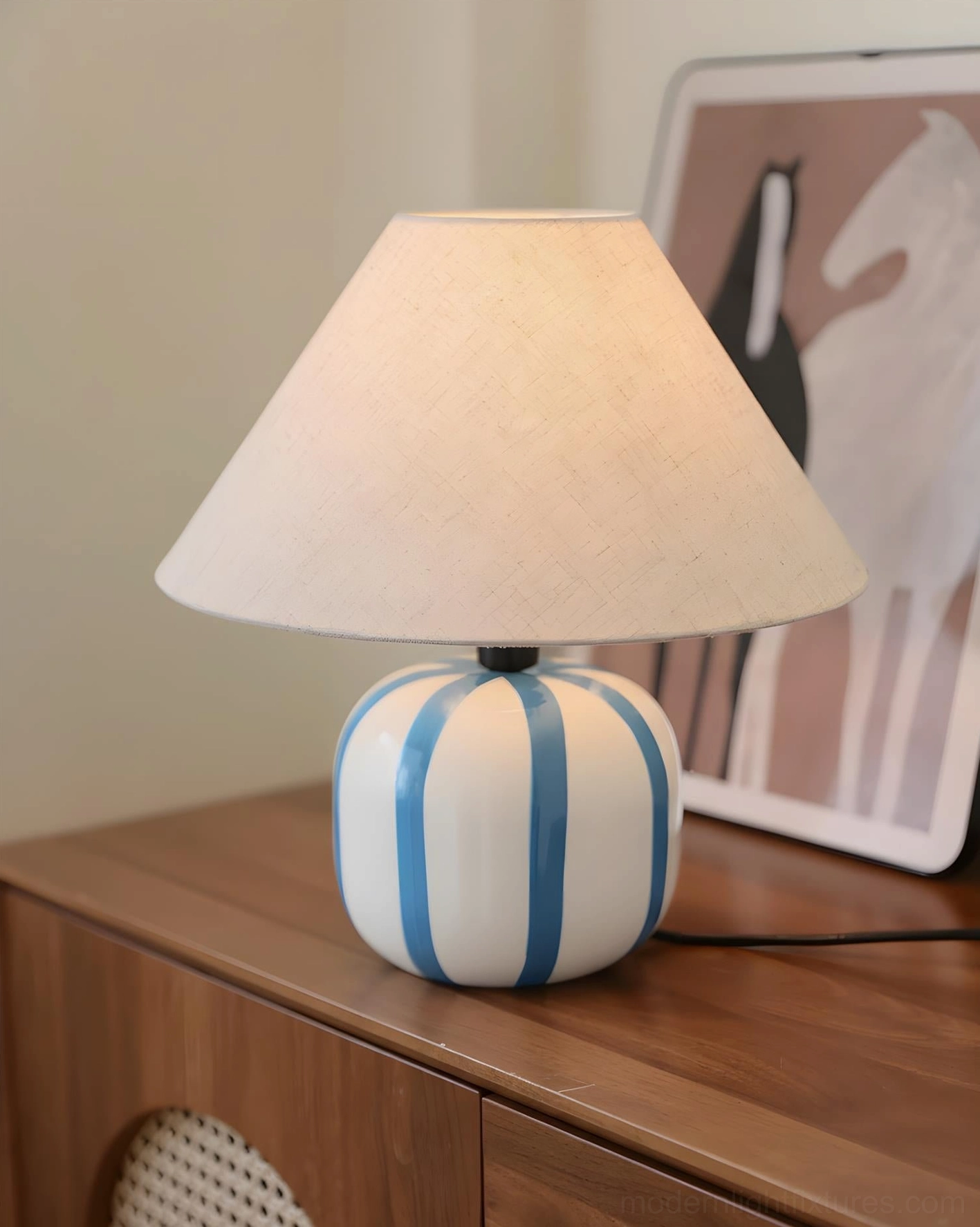 Blue and white striped spherical ceramic table lamp three-quarter view on wooden dresser