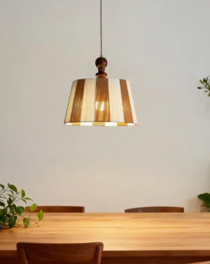 Striped pendant lamp hanging in residential dining room above table with potted houseplants, warm striping with wood hardware
