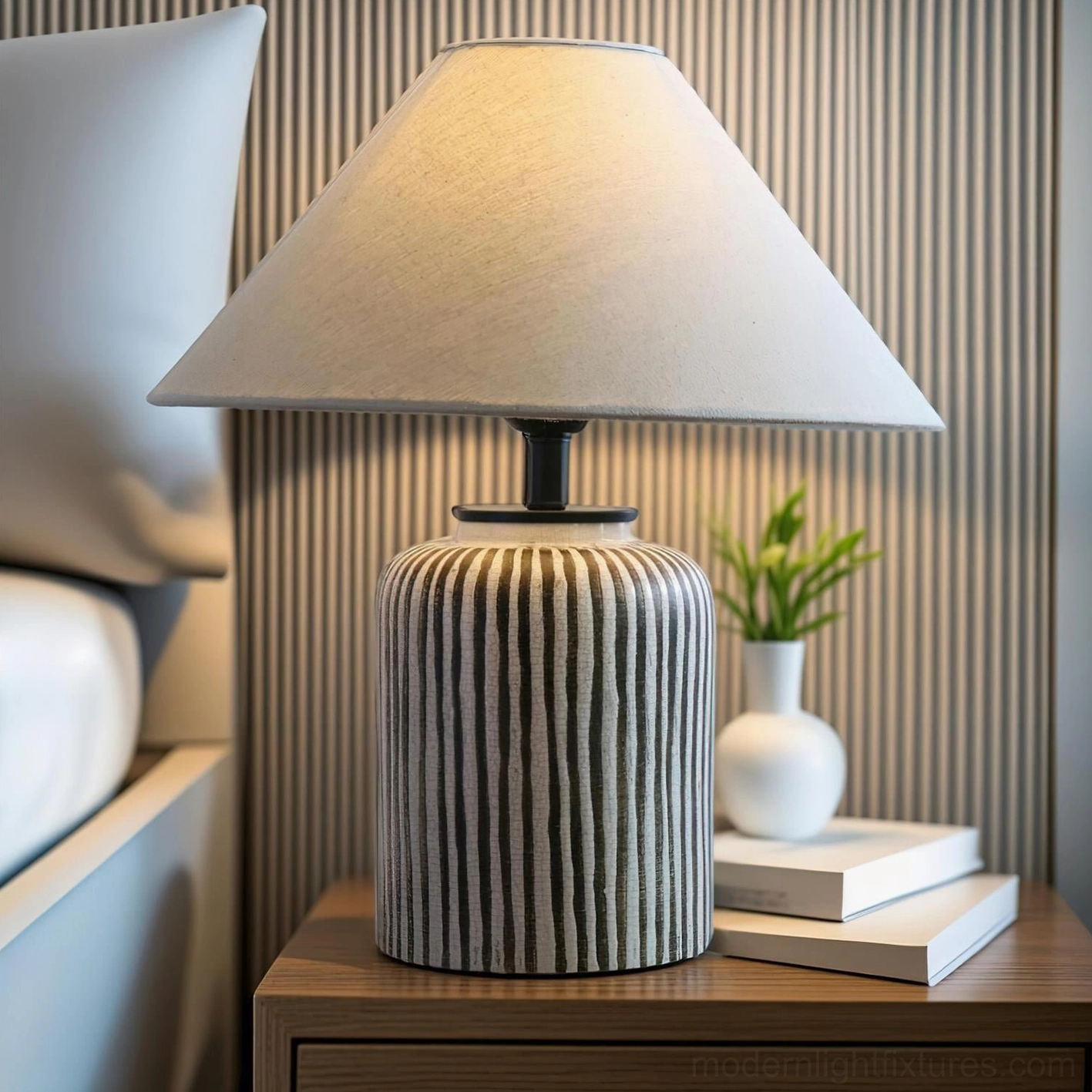 Vertical striped ceramic lamp on bedside nightstand with stacked books and potted plant styling