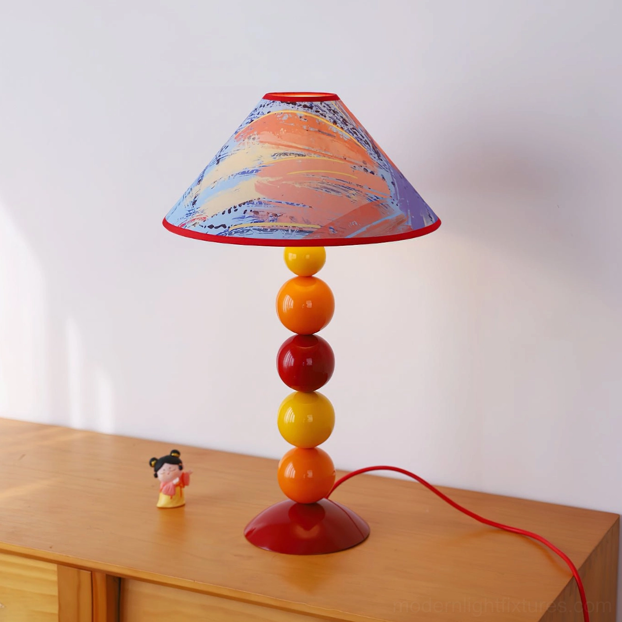 Pink-orange watercolor printed decorative table lamp with warm beaded base on wooden nightstand - eclectic interior design