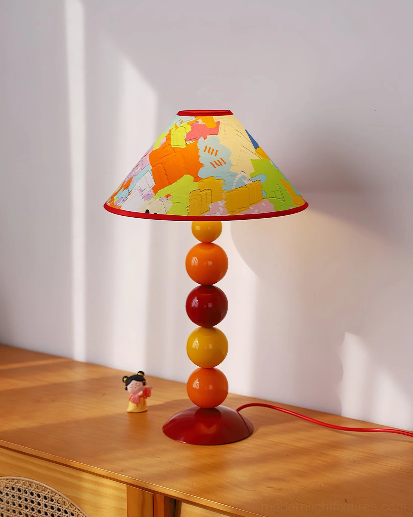 Colorful beaded table lamp displayed on wooden side table with decorative figurine and red power cord - bohemian interior styling