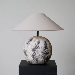 Modern Surya table lamp three-quarter front perspective - weathered ceramic base with wabi-sabi mottled finish on black display stand