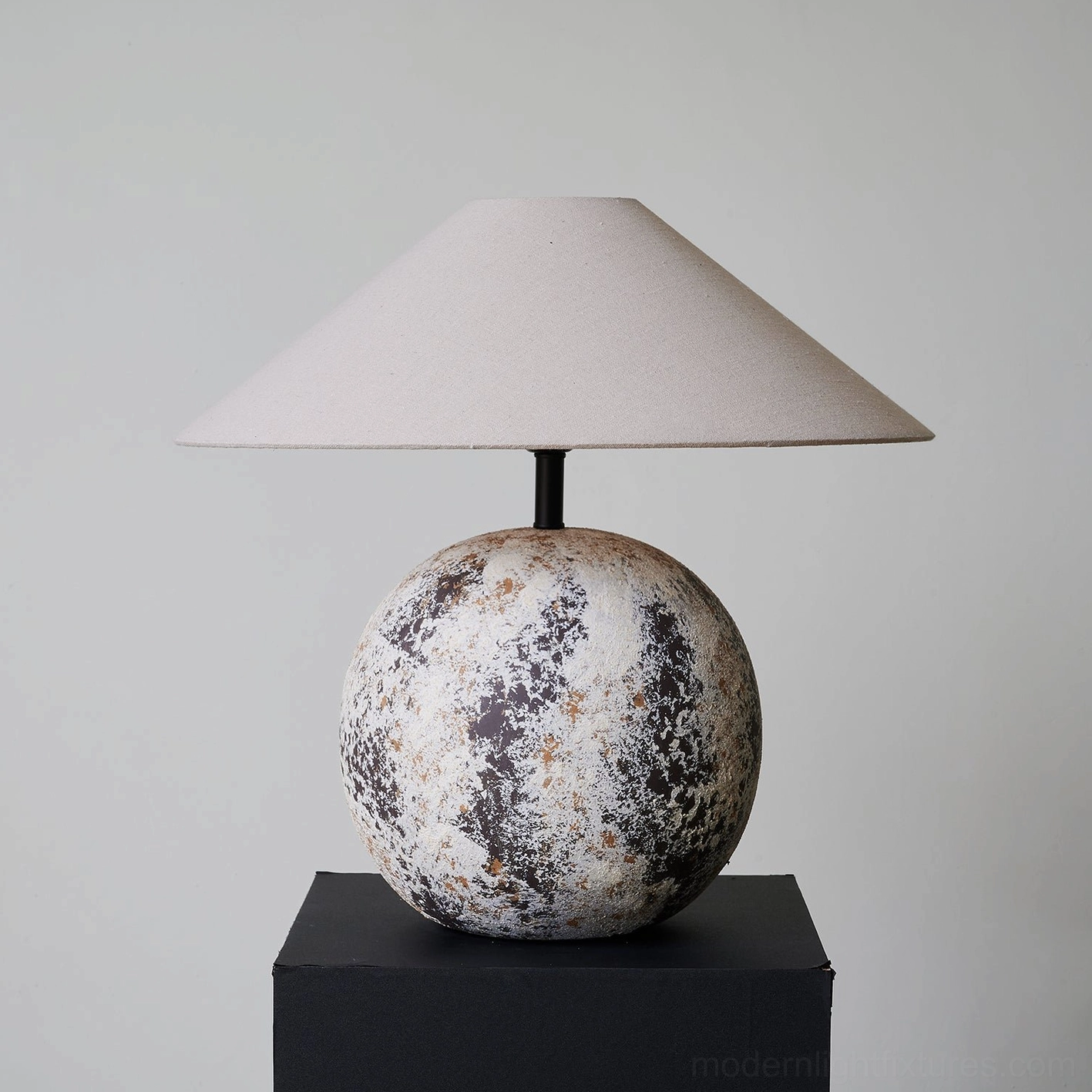 Modern Surya table lamp three-quarter front perspective - weathered ceramic base with wabi-sabi mottled finish on black display stand