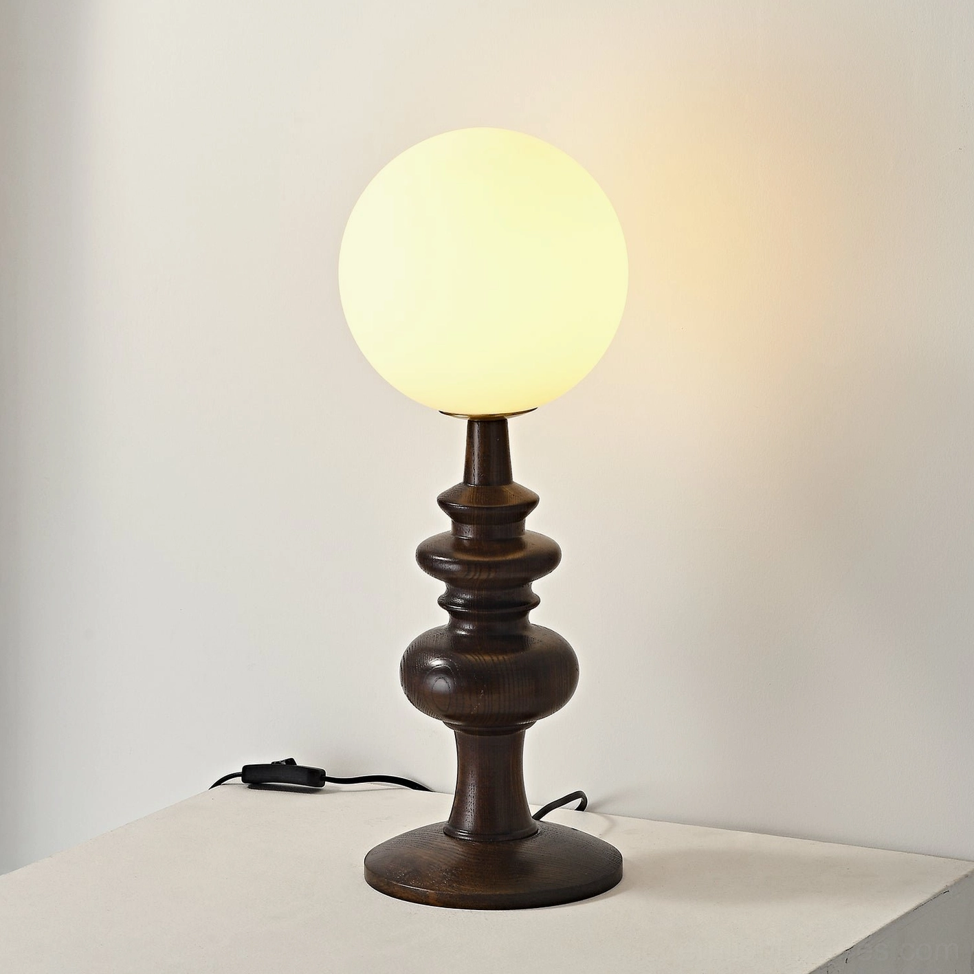 Scandinavian-style Sveta globe table lamp with dark wood base glowing warm light and visible power cable
