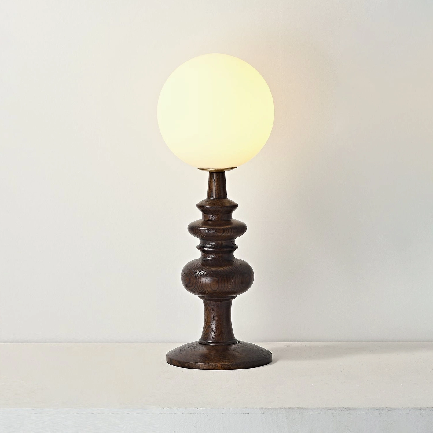 Modern Sveta table lamp lit with warm ambient glow - walnut wood turned base with illuminated frosted glass globe
