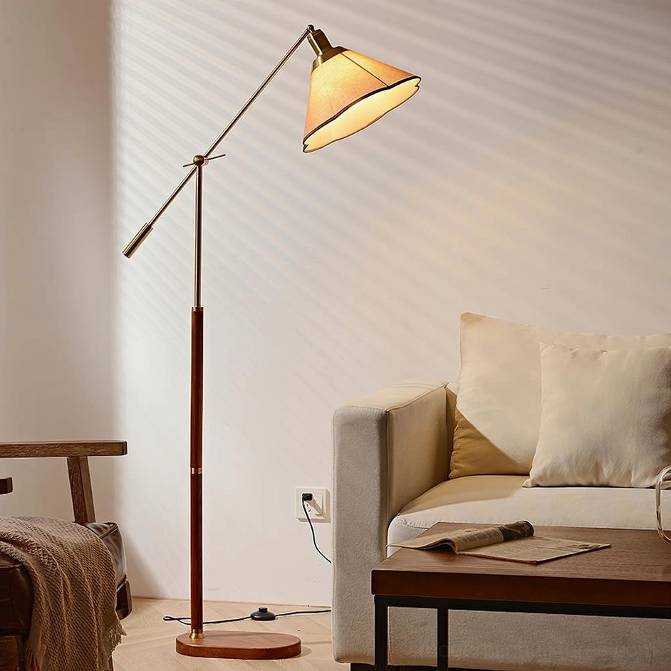 Swing arm floor lamp three-quarter side view with walnut wood pole, brass metal arm, and illuminated fabric lampshade in living room