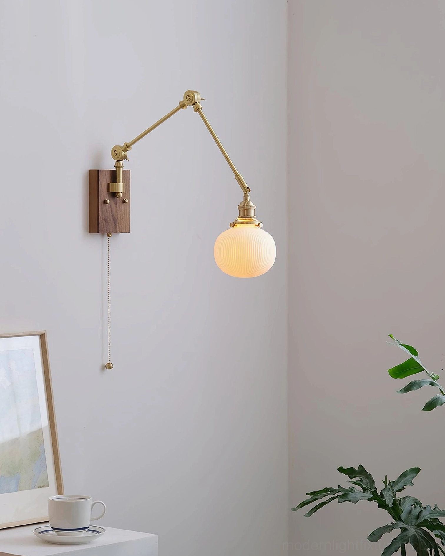Brass swing arm wall sconce with smooth ceramic shade, interior residential setting with plants and decor