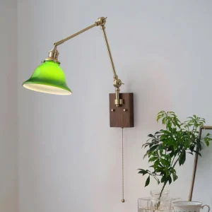 Swing arm wall light with green glass shade and brass hardware mounted on walnut wood, angled view showing adjustable arm and pull cord switch in home interior