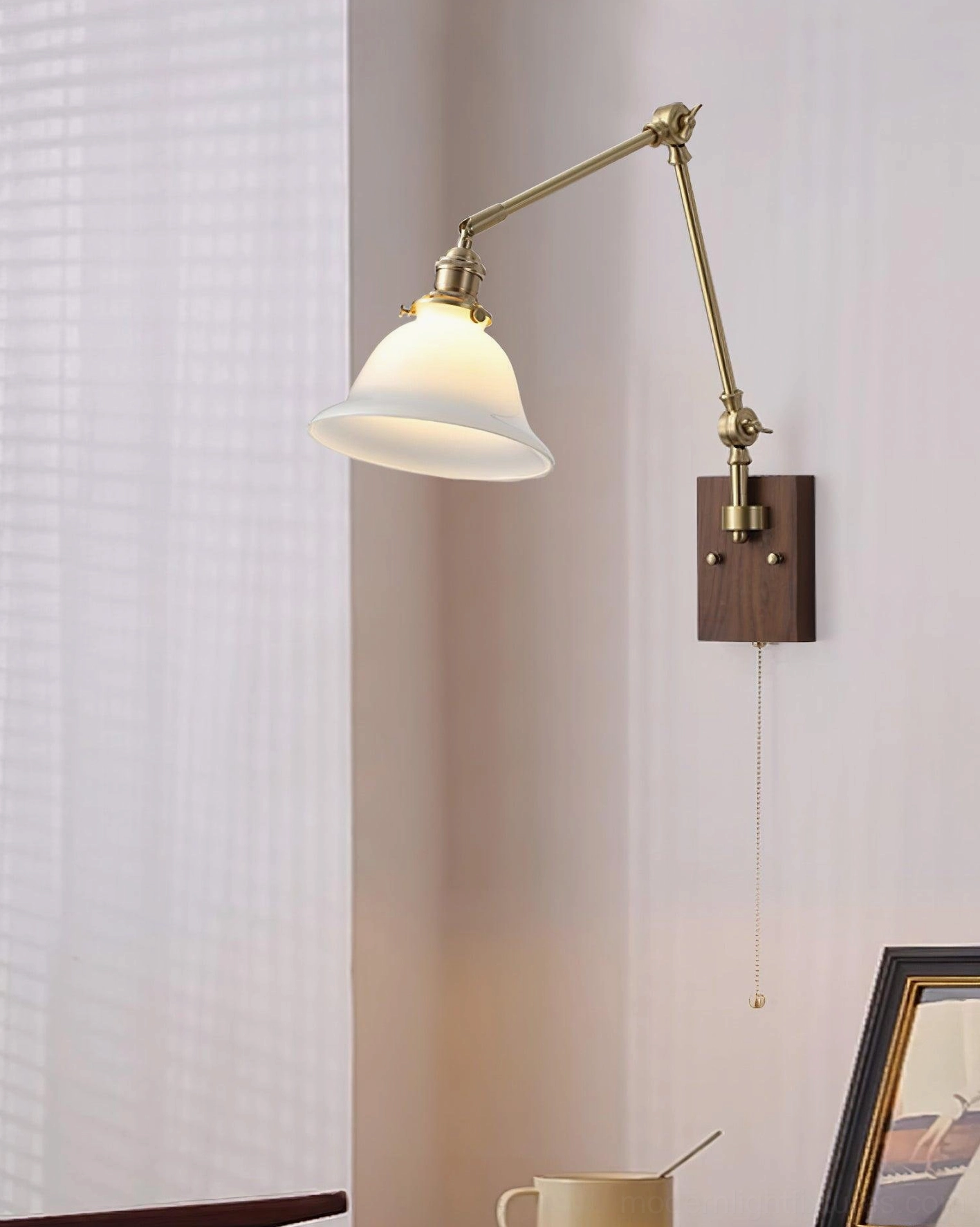 Swing arm wall lamp with white glass dome shade and brass metal arms, dark wood backplate with pull chain, angled view against sheer curtain in bedroom
