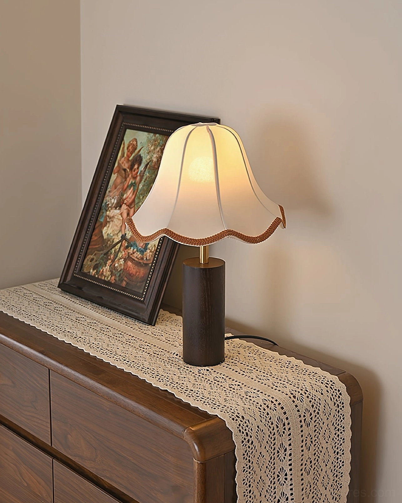 Lit table lamp with glowing scalloped shade on wooden dresser with full lace table runner classic style