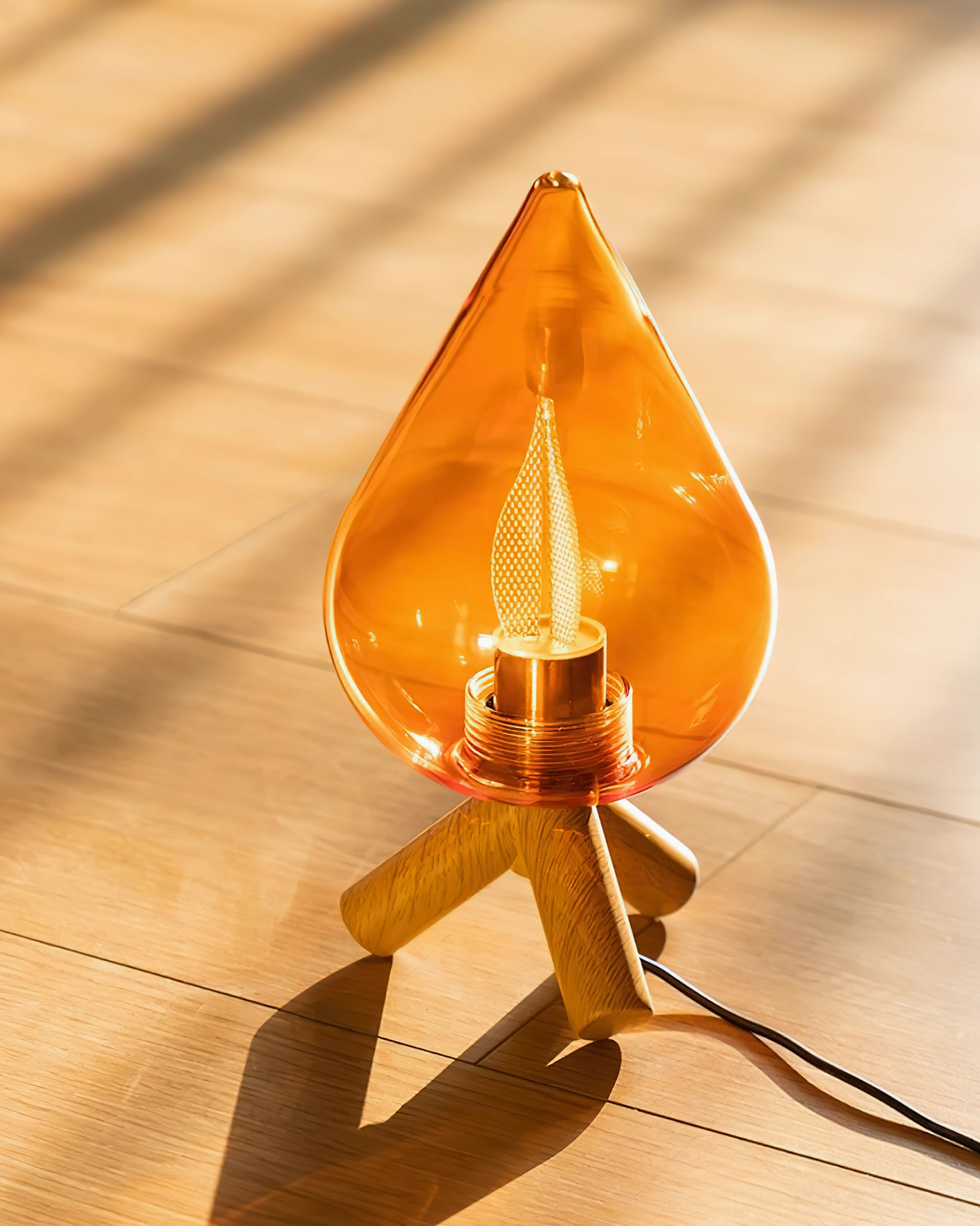 Low-angle front view of teardrop glass lamp on hardwood floor with natural sunlight creating soft shadows around amber shade and wooden tripod