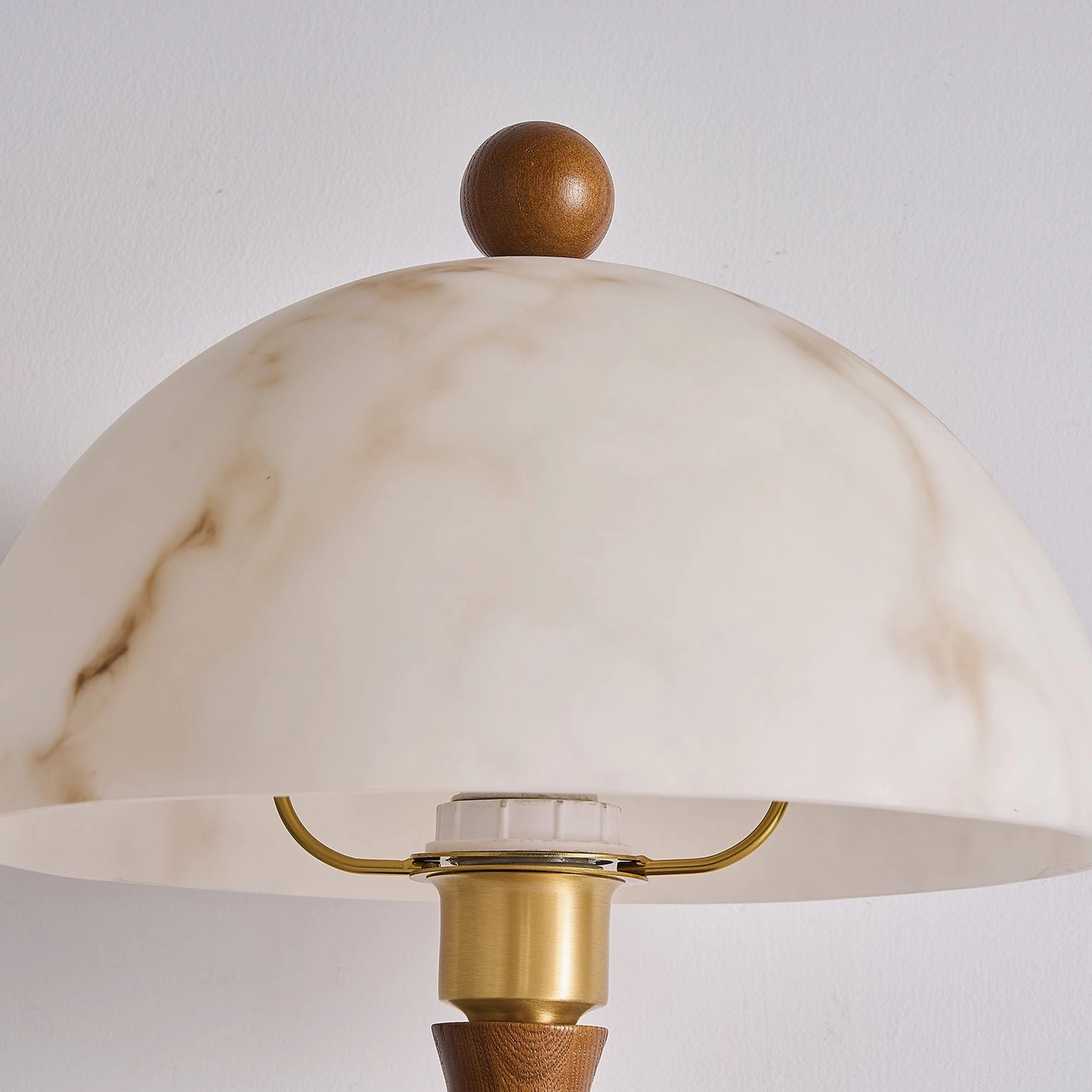 Close-up of faux alabaster dome shade assembly with brass socket fitting and wooden finial top, architectural detail view