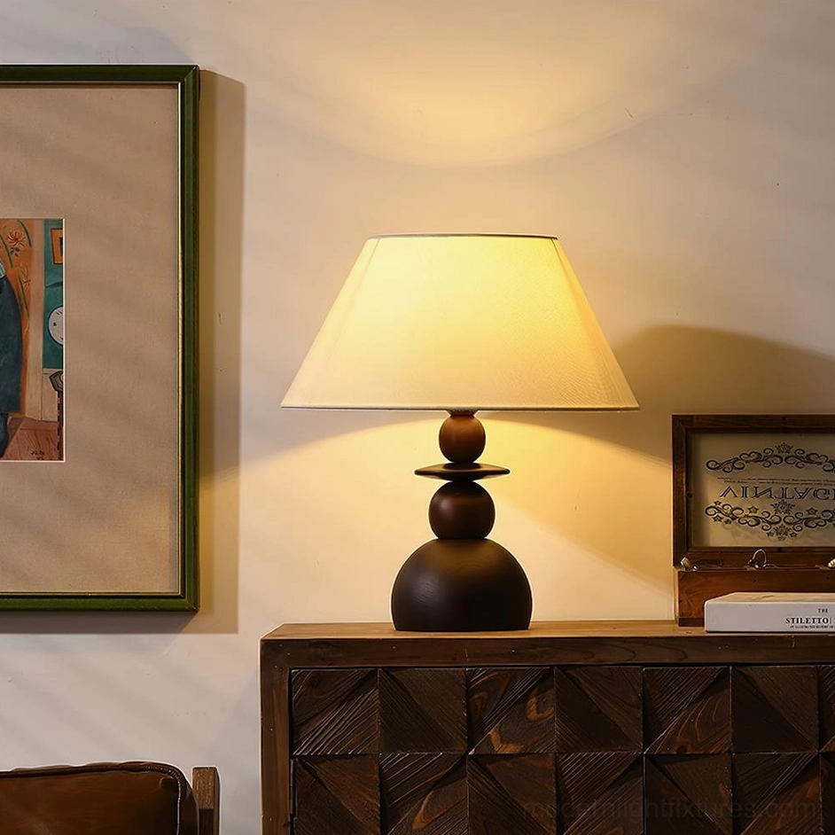 Walnut wood table lamp with beige fabric shade emitting warm glow beside framed wall art