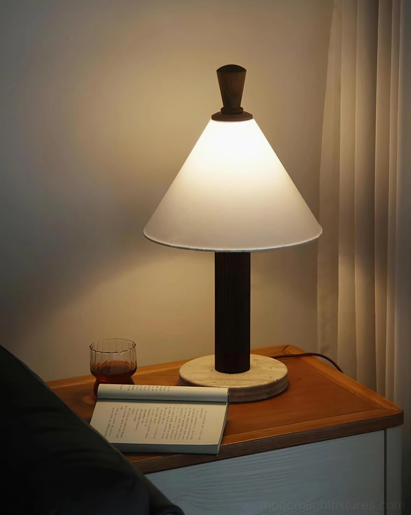 Lit Takumi lamp on living room side table with dark wood, warm ambient light, book and beverage styling