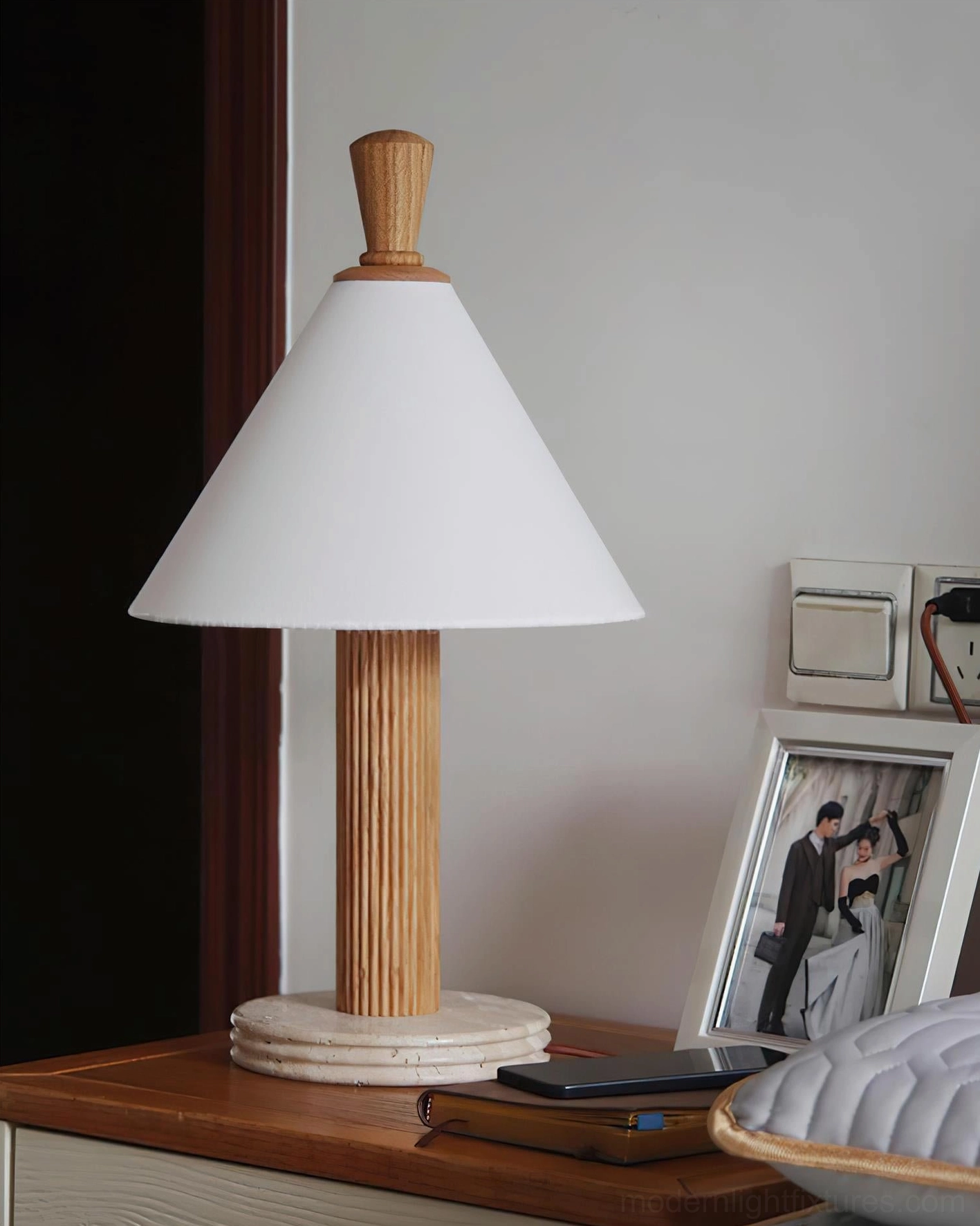 Lit Takumi table lamp on bedroom nightstand with natural fluted wood, desk accessories, and photo frame