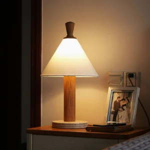 Lit Takumi table lamp on bedroom nightstand with warm glow, photo frame, and warm-toned wood finish
