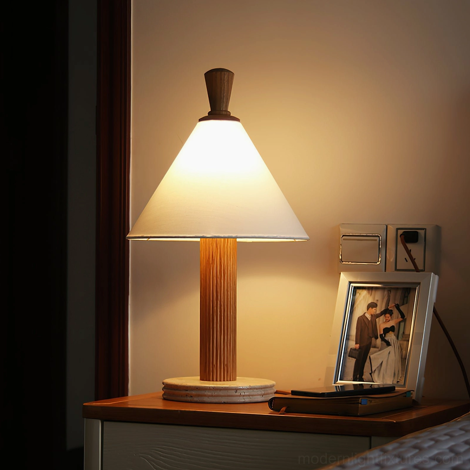 Lit Takumi table lamp on bedroom nightstand with warm glow, photo frame, and warm-toned wood finish