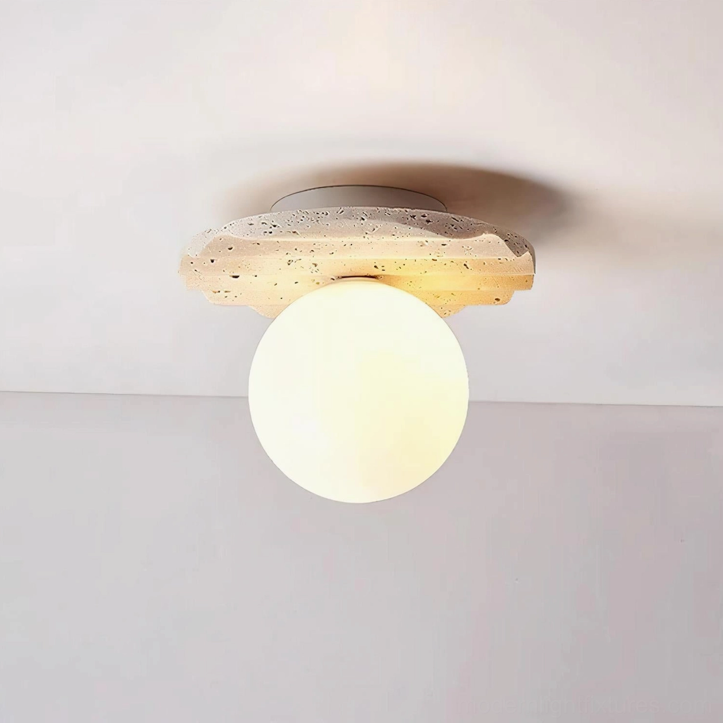 Lit Talia ceiling light fixture showcasing spotted natural travertine base with glowing warm yellow glass sphere