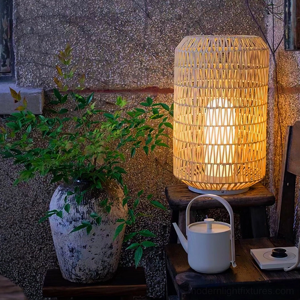 Tall cylindrical woven rattan outdoor lamp displayed at eye-level in corner garden setting with potted plants