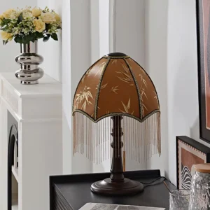 Tassel table lamp three-quarter view in vintage home living room setting with brown fabric shade and decorative accents