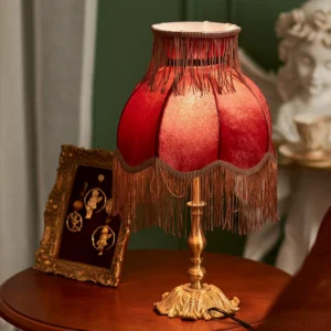 Handcrafted tassel table lamp with deep red velvet shade and decorative brass base on wooden side table