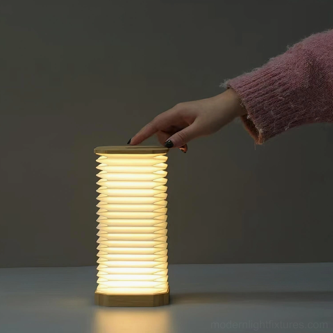 Tawa Fold accordion table lamp side view with hand adjusting power switch warm glowing light
