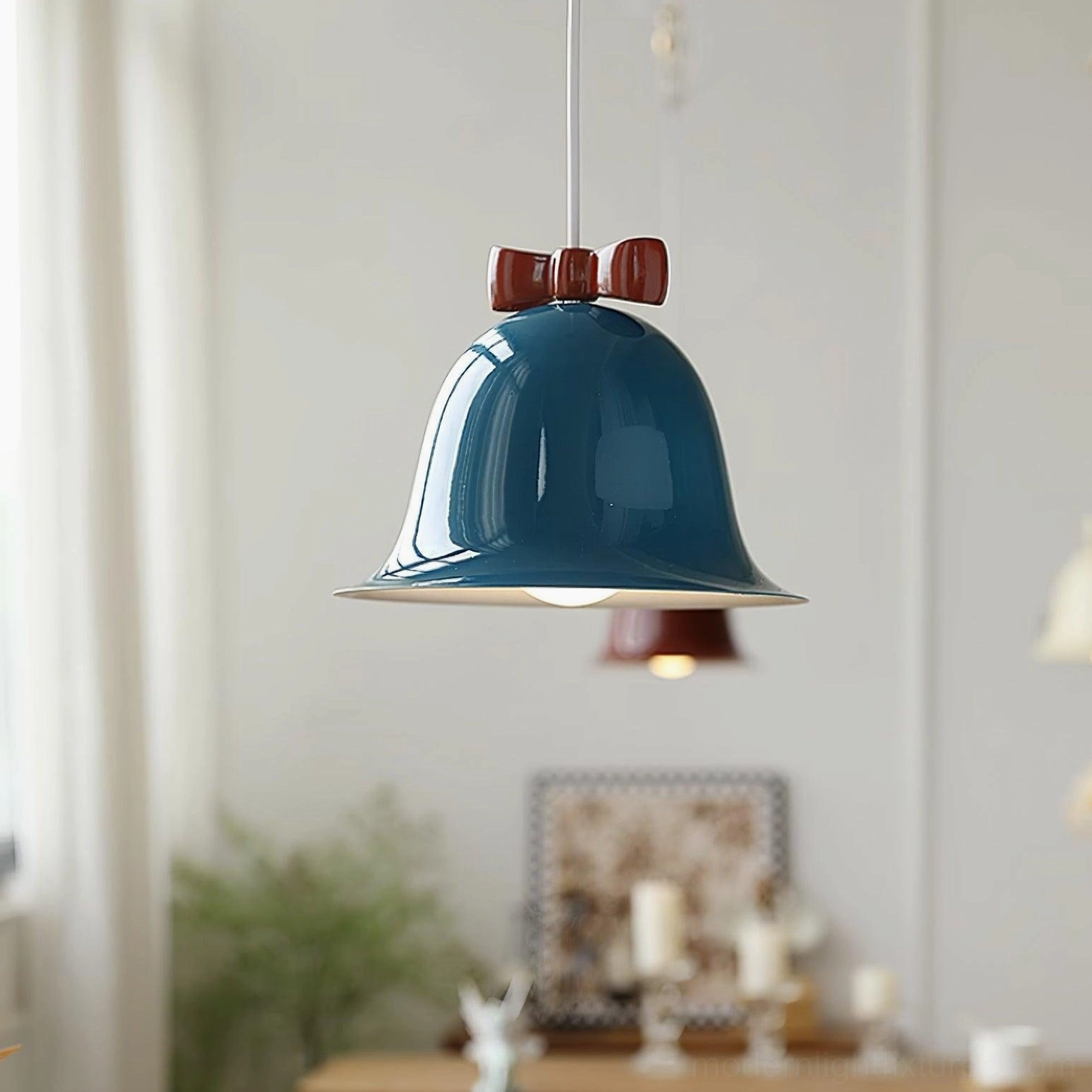 Teal blue glossy bell-shaped pendant light with brown bow hanging in bright dining room with sheer curtains