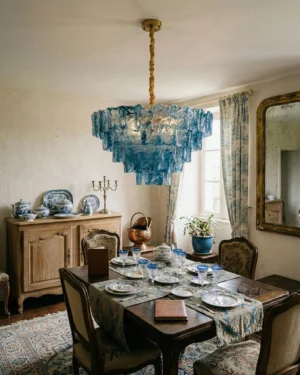 Teal blue modern tiered glass chandelier installed in formal vintage dining room, eye-level interior perspective showing pendant suspended above dining space