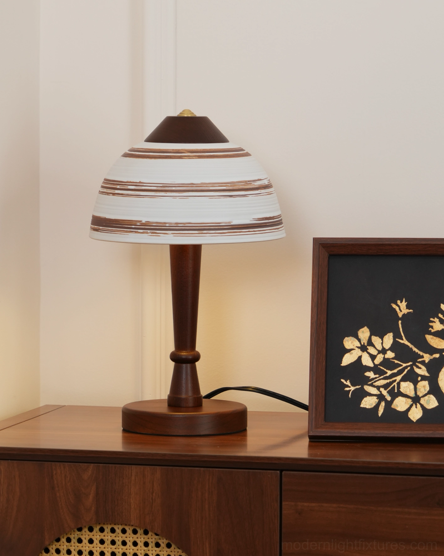 Tera ceramic wood table lamp displayed in home corner with dark wood cabinet and framed botanical artwork