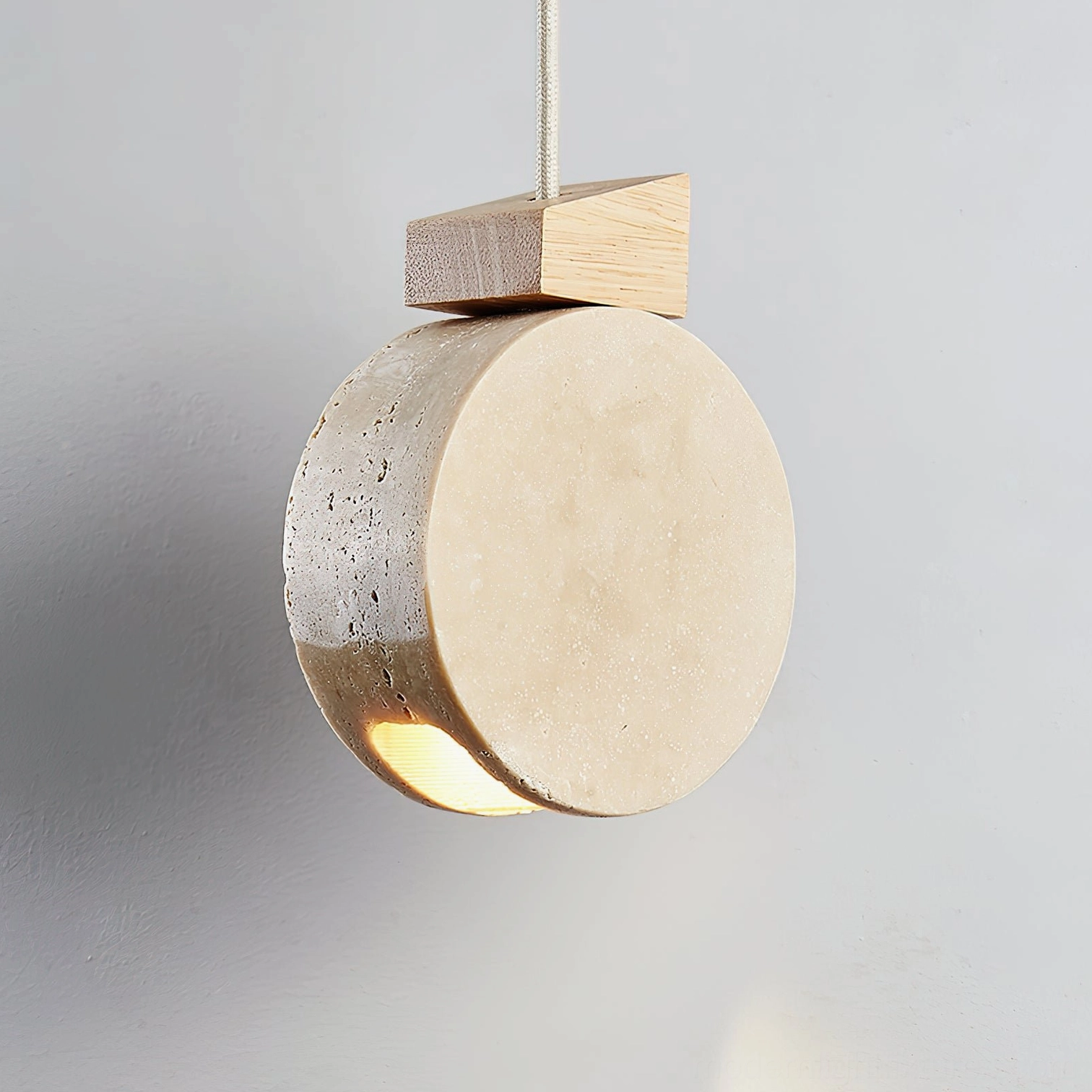 Terra Ring travertine pendant light right angle front view with light wood fixture and glowing bottom light