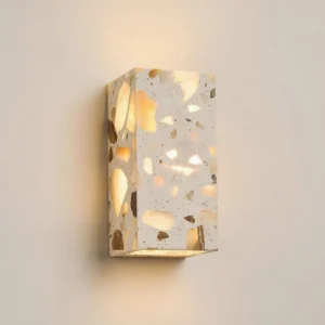 Vertical rectangle terrazzo wall sconce 8cm x 16cm in grey casting warm ambient light with three-quarter perspective showing aggregate texture detail