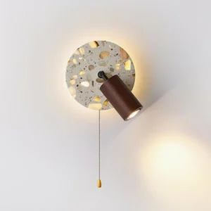 Minimalist terrazzo wall sconce three-quarter view with warm backlit glow highlighting textured aggregate finish
