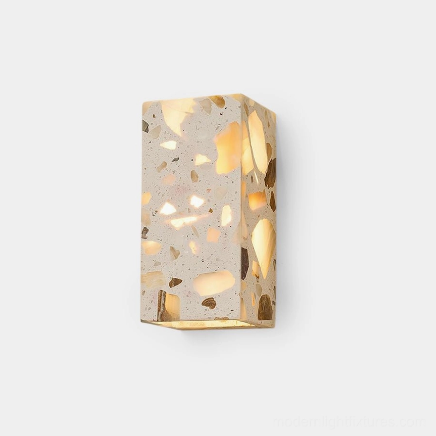 Terrazzo wall sconce front view with warm glowing integrated LED light casting dappled illumination from embedded natural stone fragments