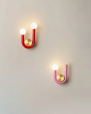 Thalia U wall sconces in red and pink macaron colors with dual-globe design and brass gold accents displayed on wall