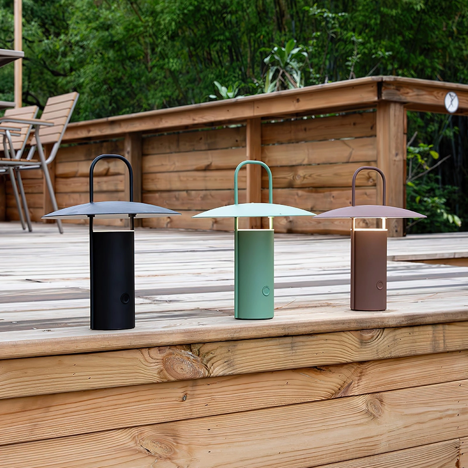 Set of three portable LED table lamps in black, mint green, and brown on outdoor wooden patio deck