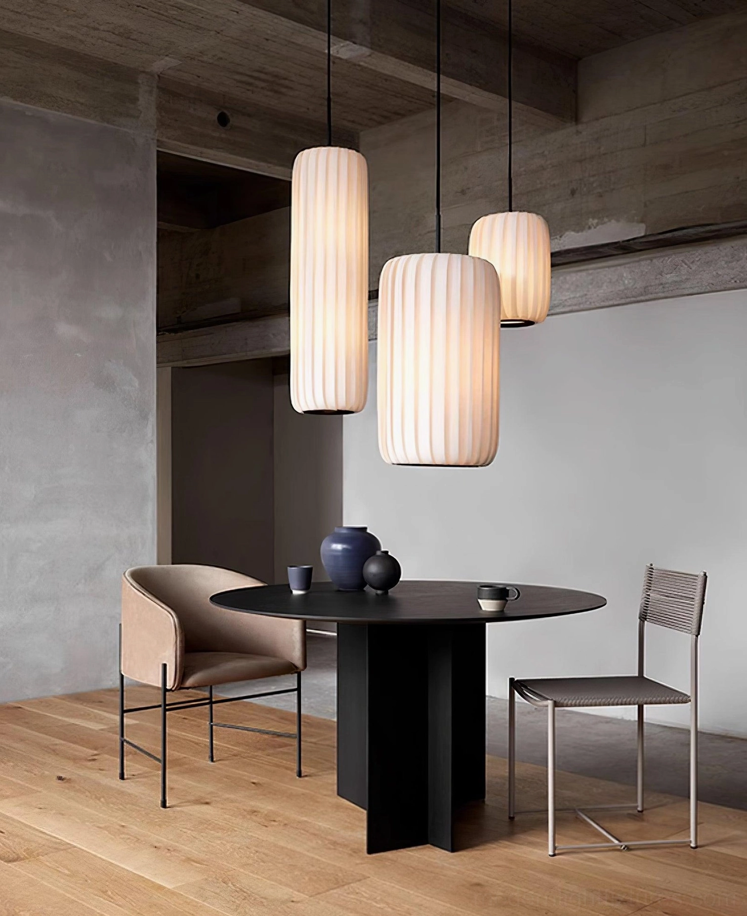 Three ribbed fabric pendant lights hanging above black round dining table on wooden floor