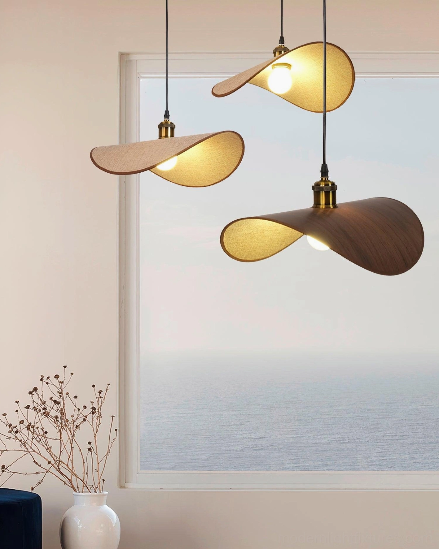 Set of three handcrafted pendant lights above minimalist table with coastal sea view window backdrop
