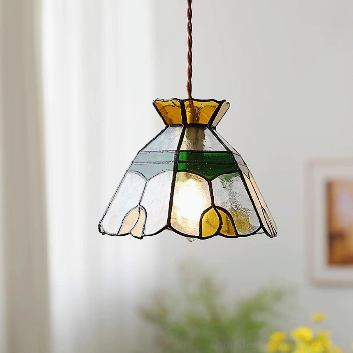 Illuminated Tiffany stained glass pendant light hanging in cozy home setting with warm amber and green glass tones, twisted brown suspension cord