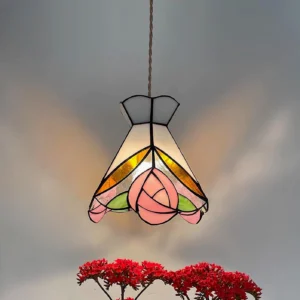 Close-up of illuminated Tiffany rose pendant lamp showing detailed stained glass rose petals and warm glow against red floral backdrop