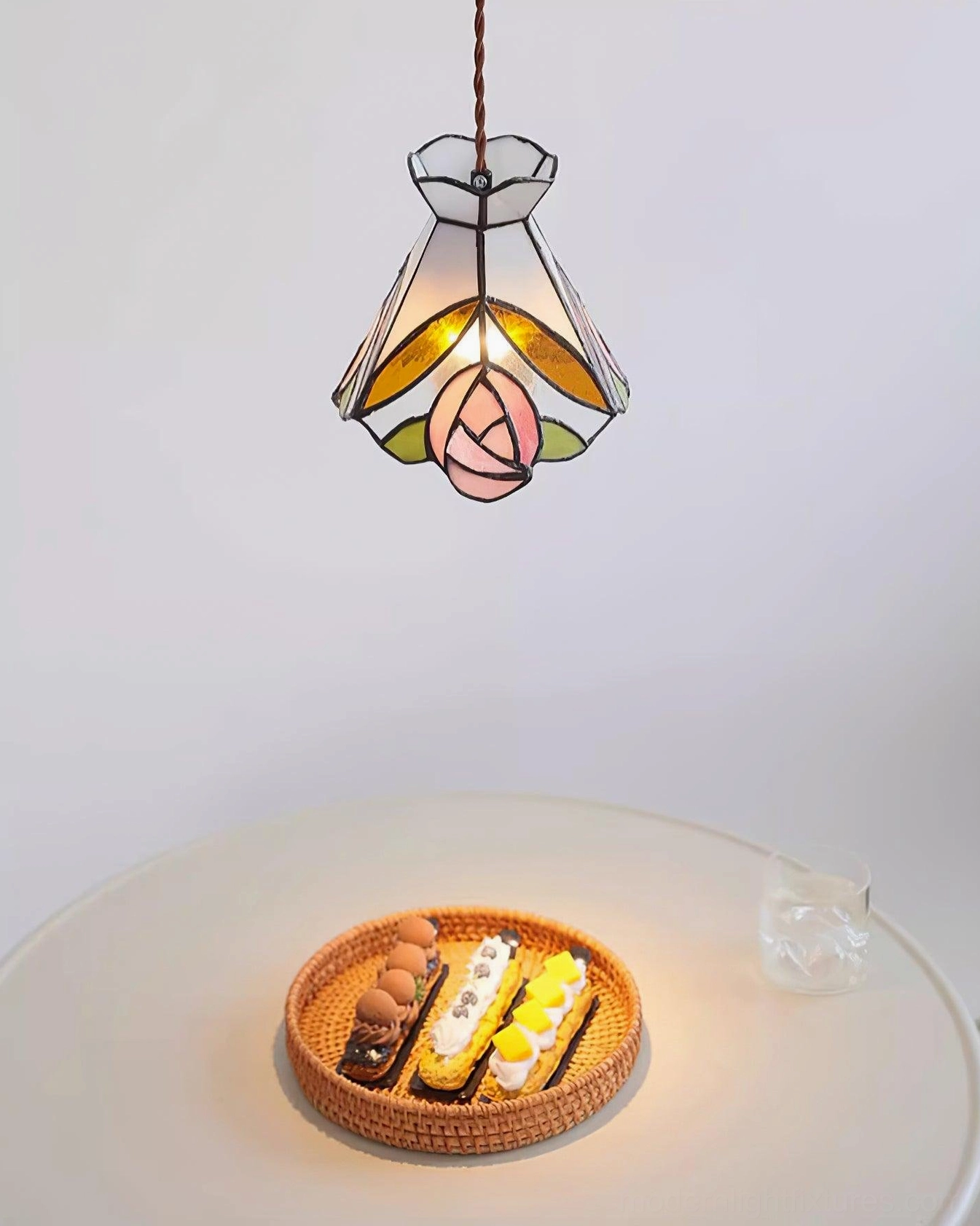 Overhead view of illuminated Tiffany rose stained glass pendant above elegant white round dining table
