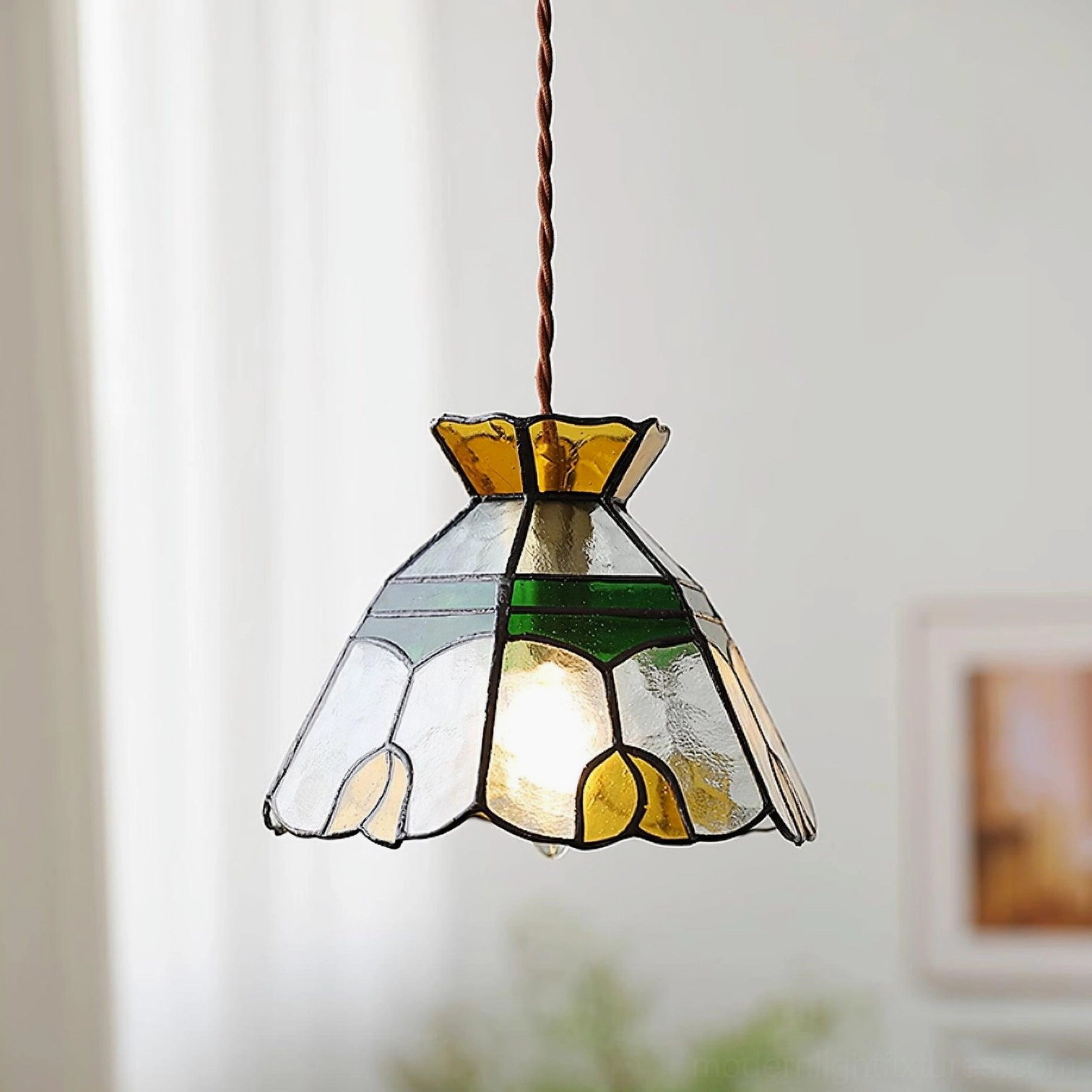 Tiffany stained glass hanging pendant light glowing with exposed bulb, green and amber colored glass panels in bedroom or living room decor