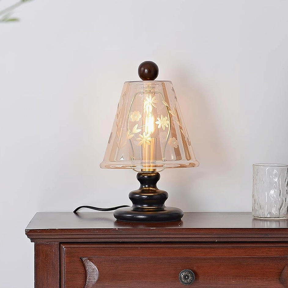 Black walnut Tilda table lamp with lit filament bulb, three-quarter view showing warm amber glow on bedroom dresser